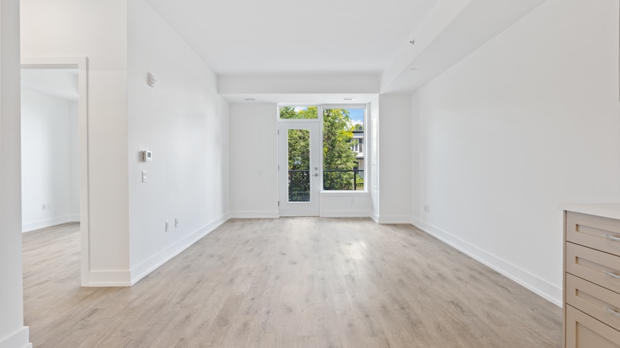 empty bright apartment room with pale wood flooring and a window at the far end
